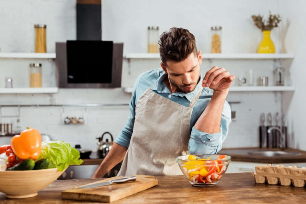  Chef Been wearing an apron and confidently seasoning a colorful bowl of fresh salad in a modern home kitchen